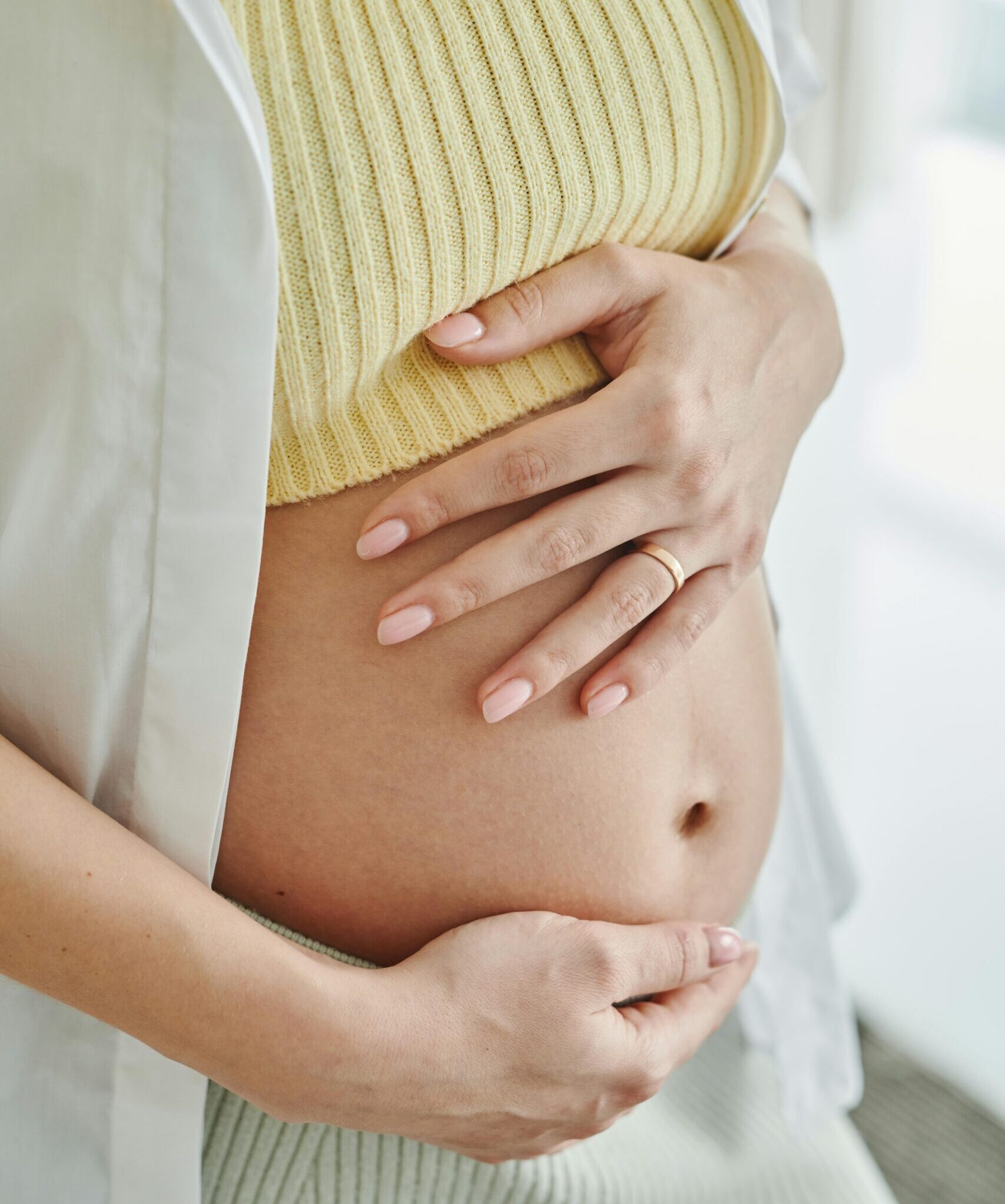 A close-up shot of a pregnant woman's hands gently resting on her belly, symbolizing motherhood.